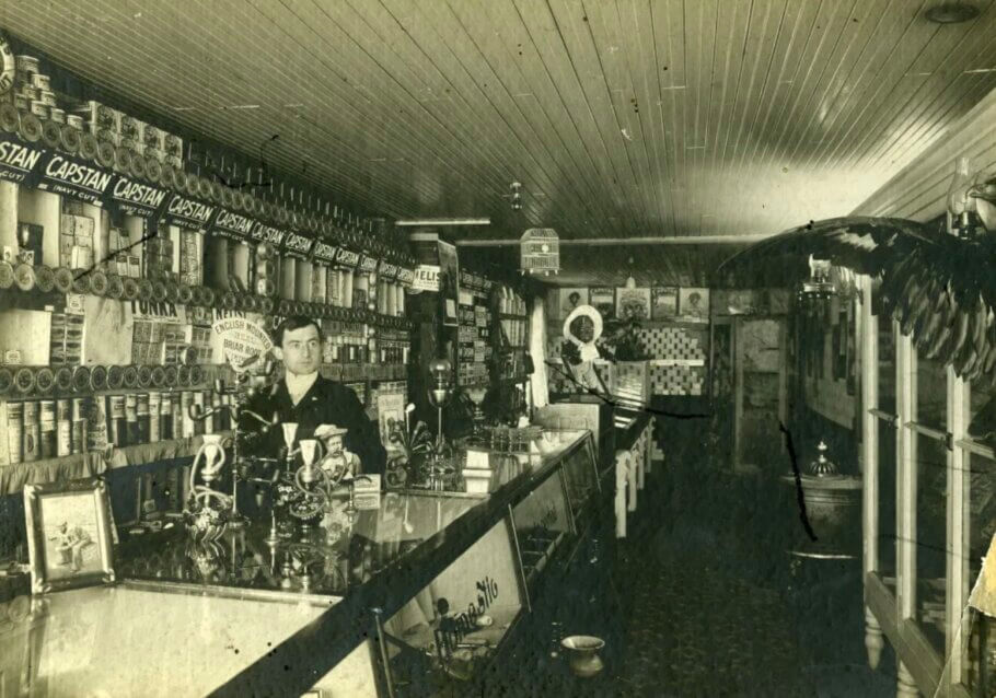 Vintage Headshop. Roy Smythe en su 'salón de billar y tienda de tabaco' vendiendo narguiles y pipas en el mostrador con pipas de opio debajo del vidrio del mostrador. Revelstoke, Columbia Británica, 1903